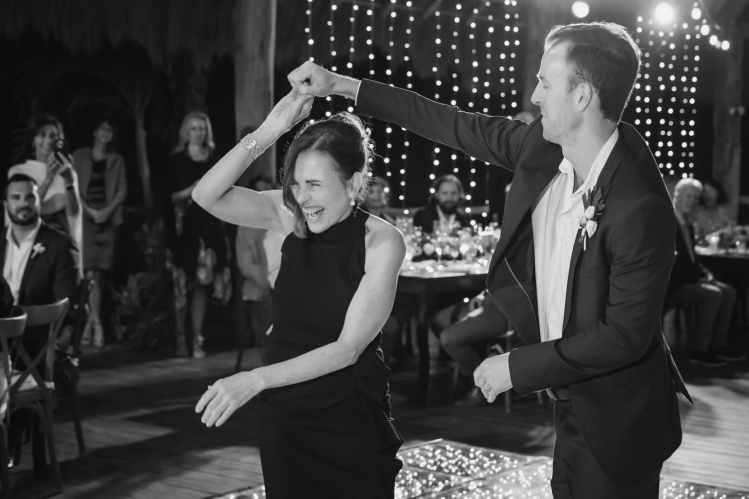 Black and white photo of a couple dancing at a wedding reception, man spinning woman on the dance floor.