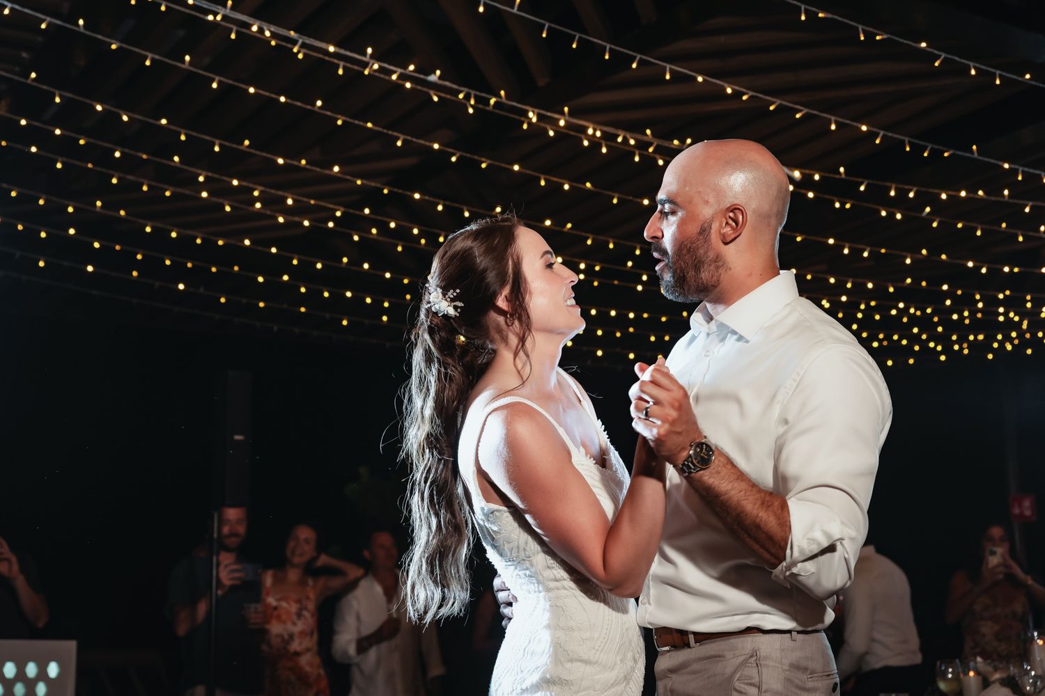 Bride and groom share their first dance under romantic string lights at their wedding reception.