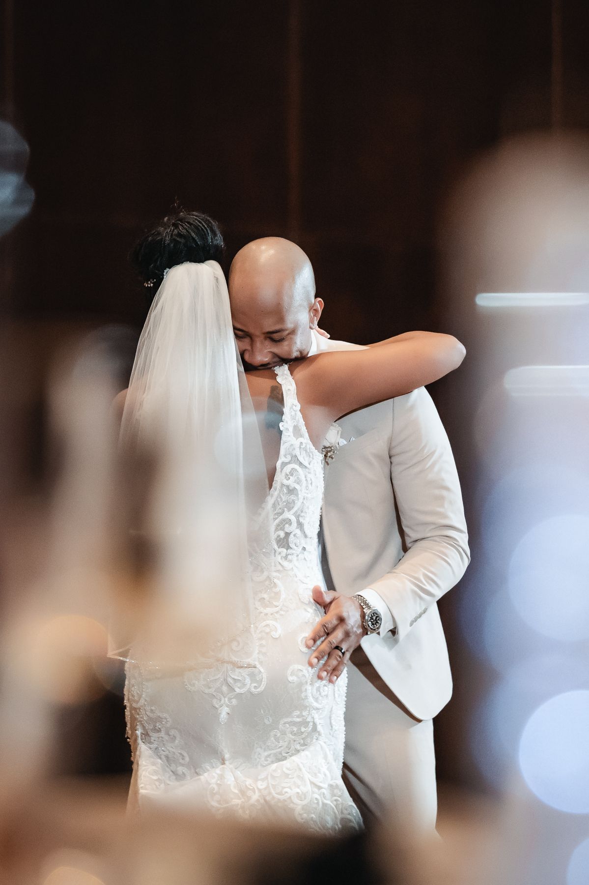 Bride and groom share an emotional first dance embrace, wearing white lace gown with veil and cream suit.