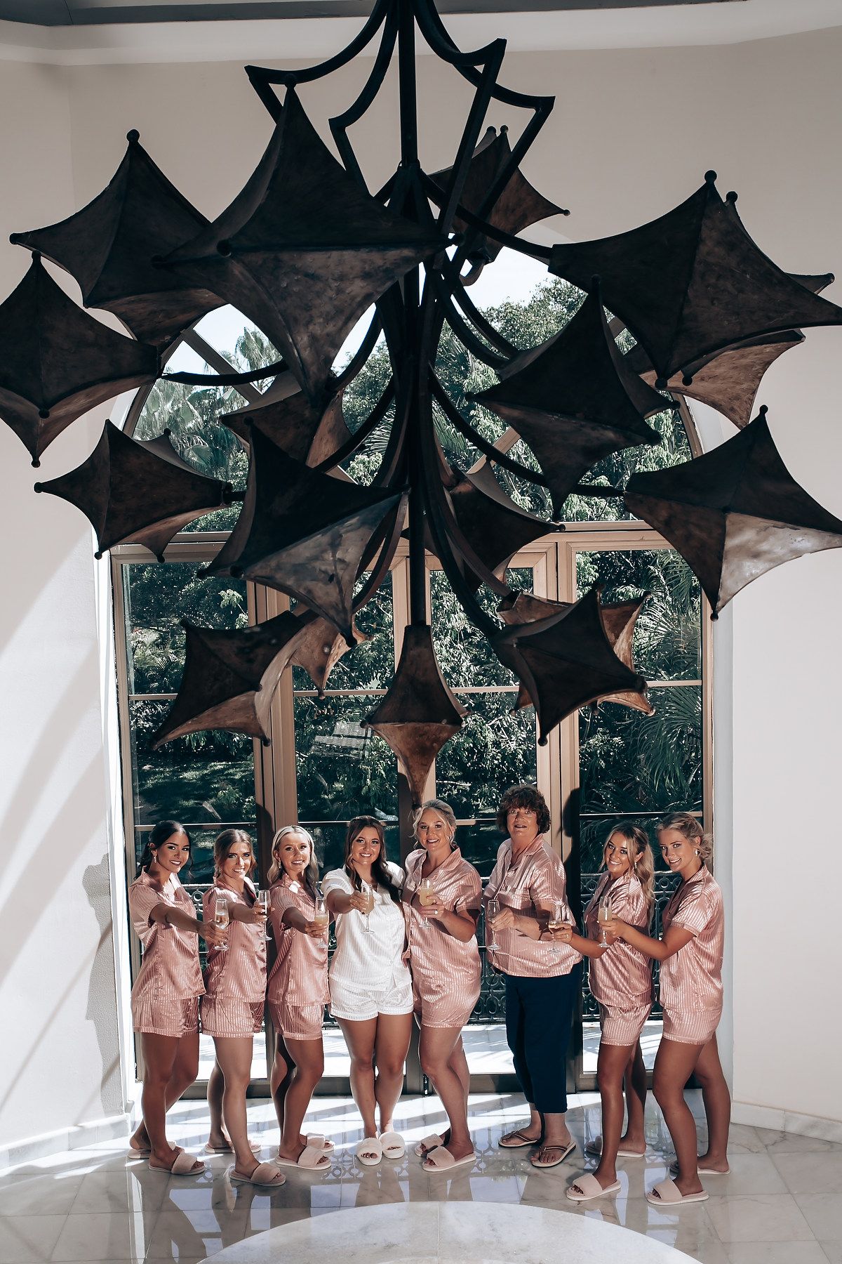 Wedding party members in matching outfits pose playfully under black decorative bats hanging from a white gazebo.