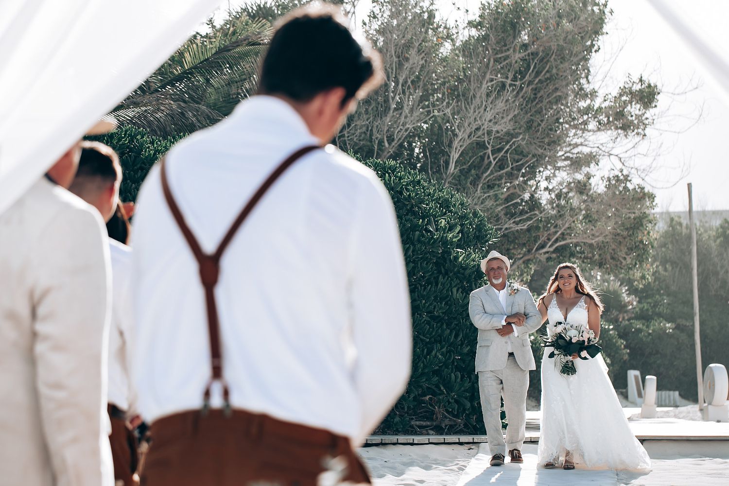 Wedding attendees in formal attire stand together outdoors.