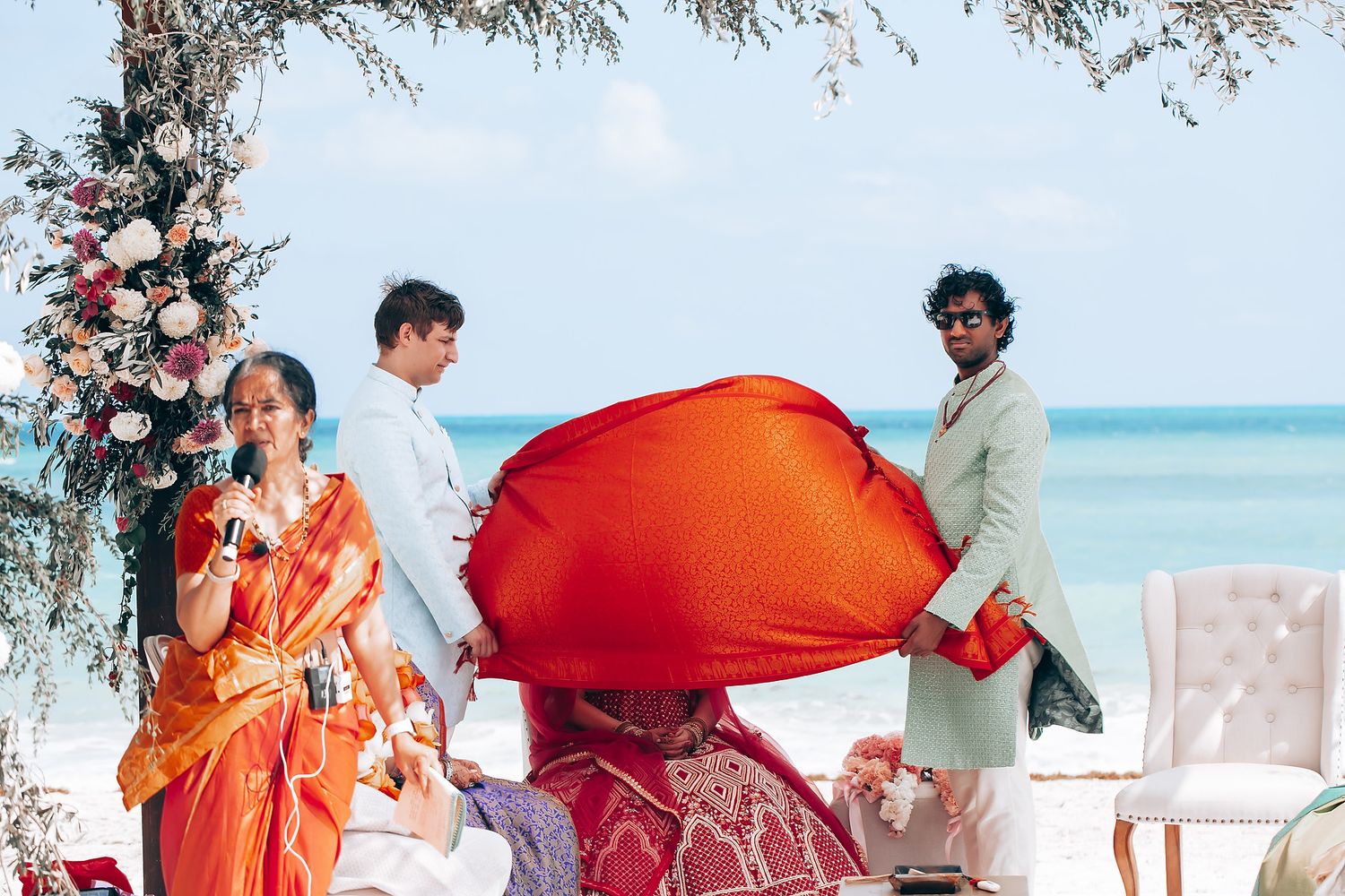 Outdoor beach wedding ceremony with flowing red fabric and floral decorations.