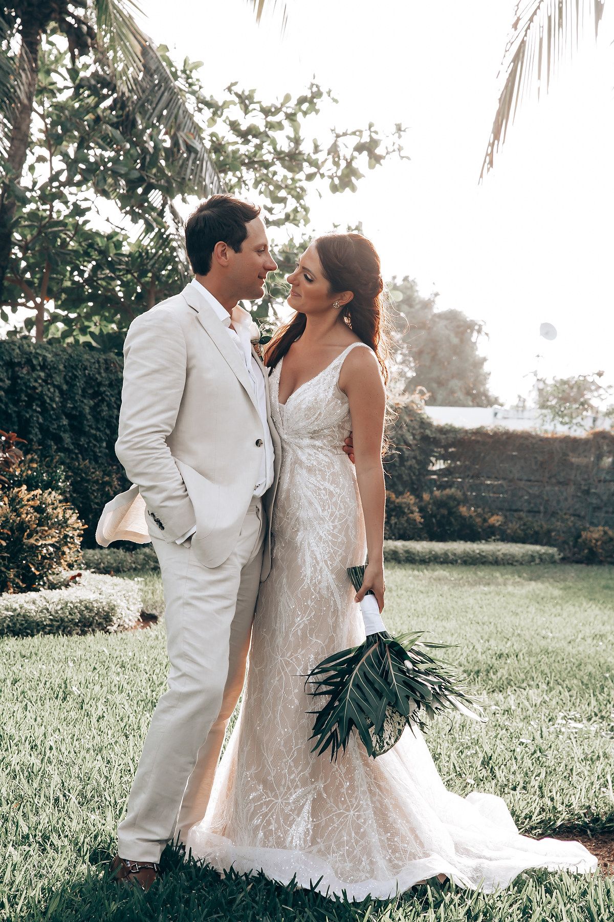 Romantic wedding portrait in a garden setting with palm trees and natural lighting.