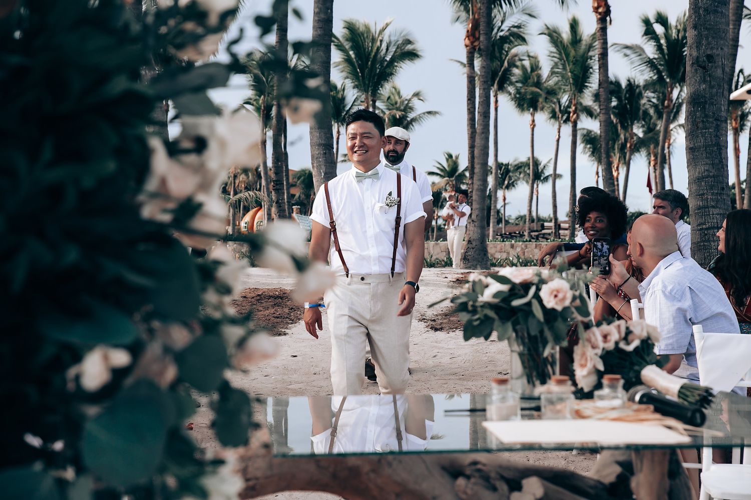 Tropical beach wedding ceremony setup with palm trees and white floral decorations.