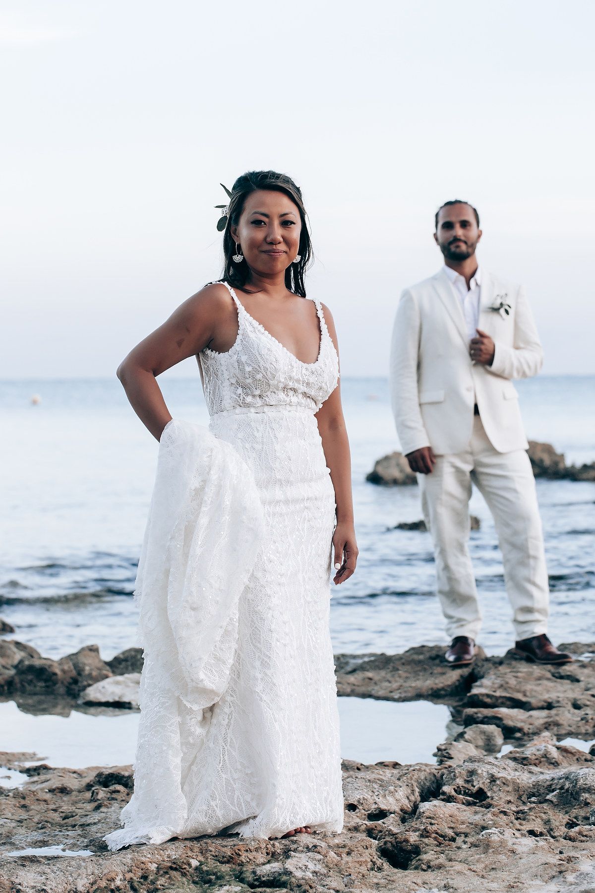 A coastal wedding photoshoot on rocky shores with waves and white attire.