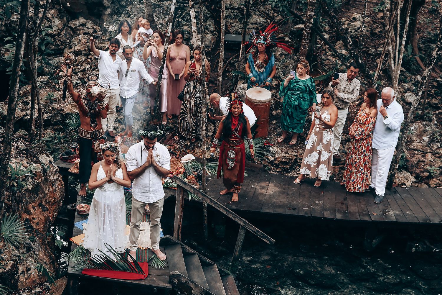 Wedding guests gather on wooden platforms overlooking a natural cenote during an outdoor ceremony.