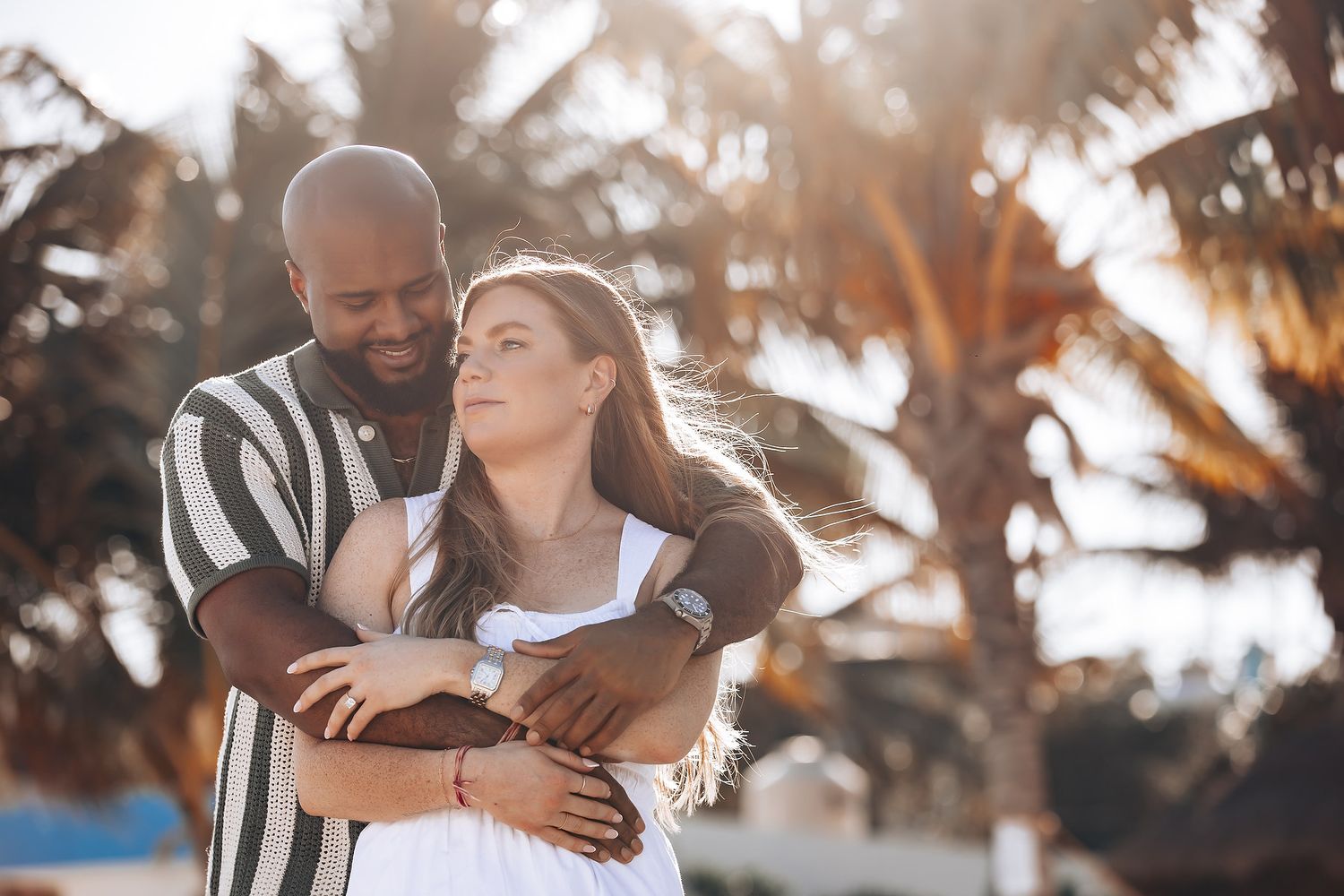 Happy interracial couple embracing on a tropical beach with palm trees in warm golden sunlight.