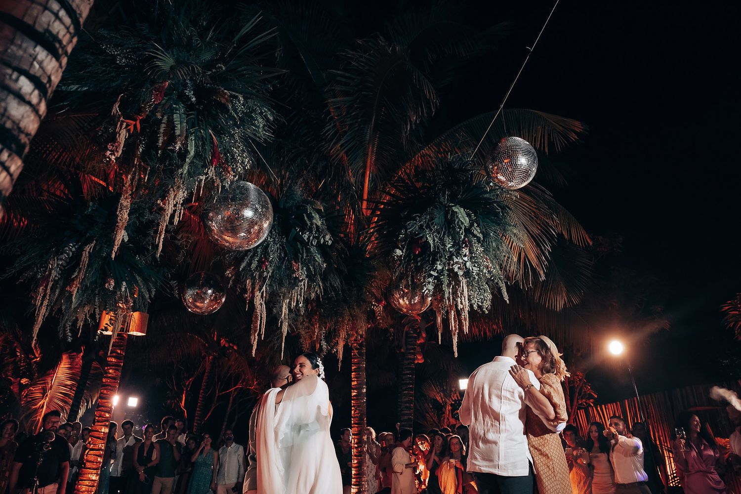 Romantic dance scene at tropical wedding reception with palm trees and mood lighting.