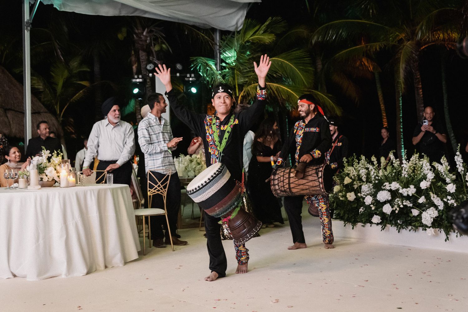 Traditional dhol drummer performs energetically at outdoor tropical wedding reception celebration.