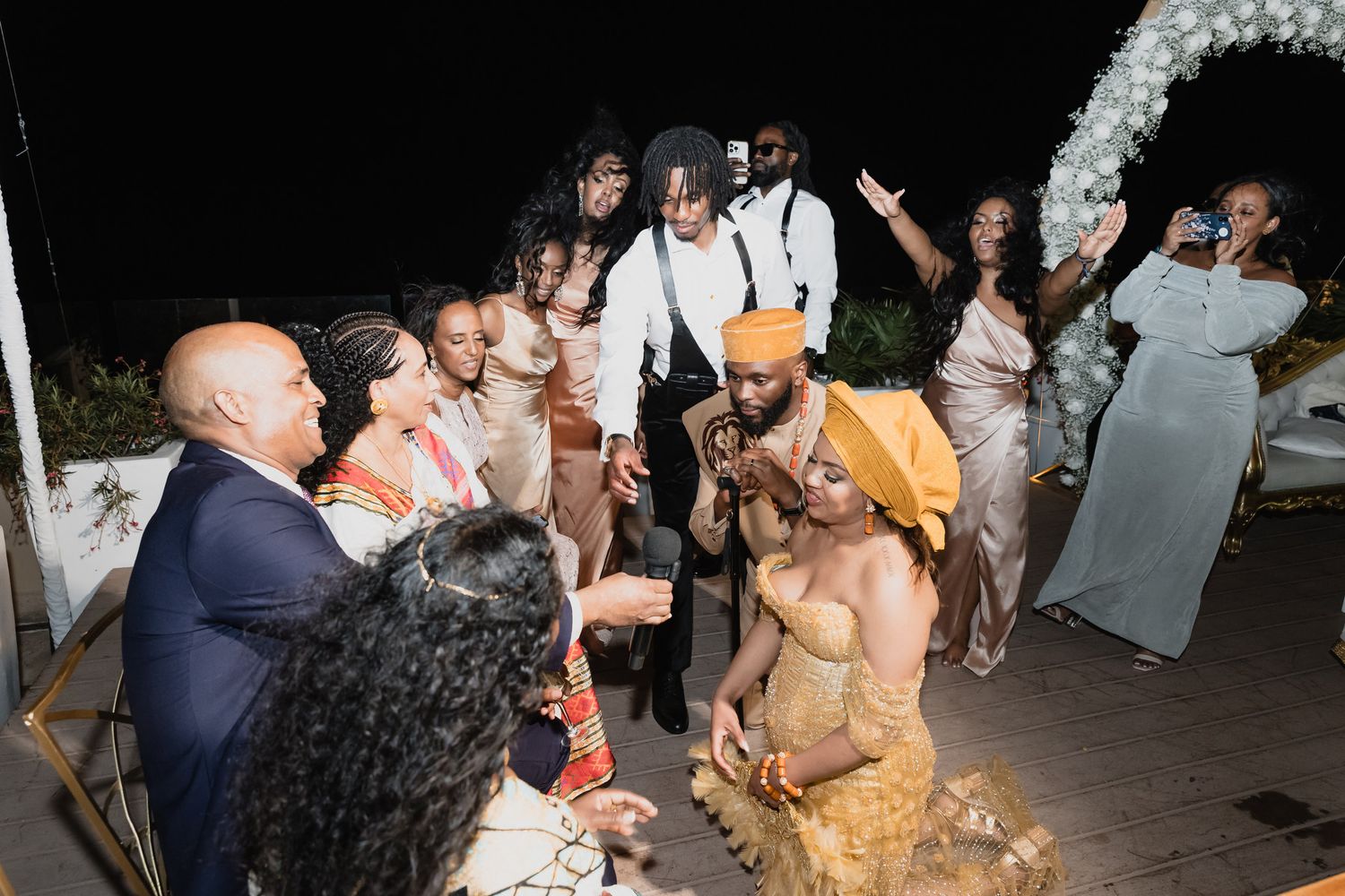 Wedding guests celebrate with bride and groom during lively outdoor nighttime reception ceremony.