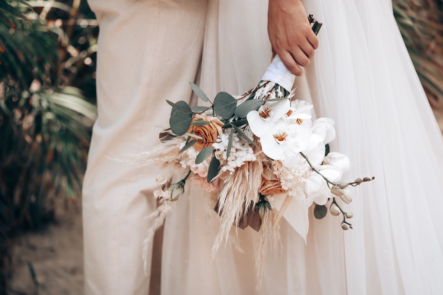An elegant wedding bouquet with white flowers and eucalyptus leaves against a flowing white dress.