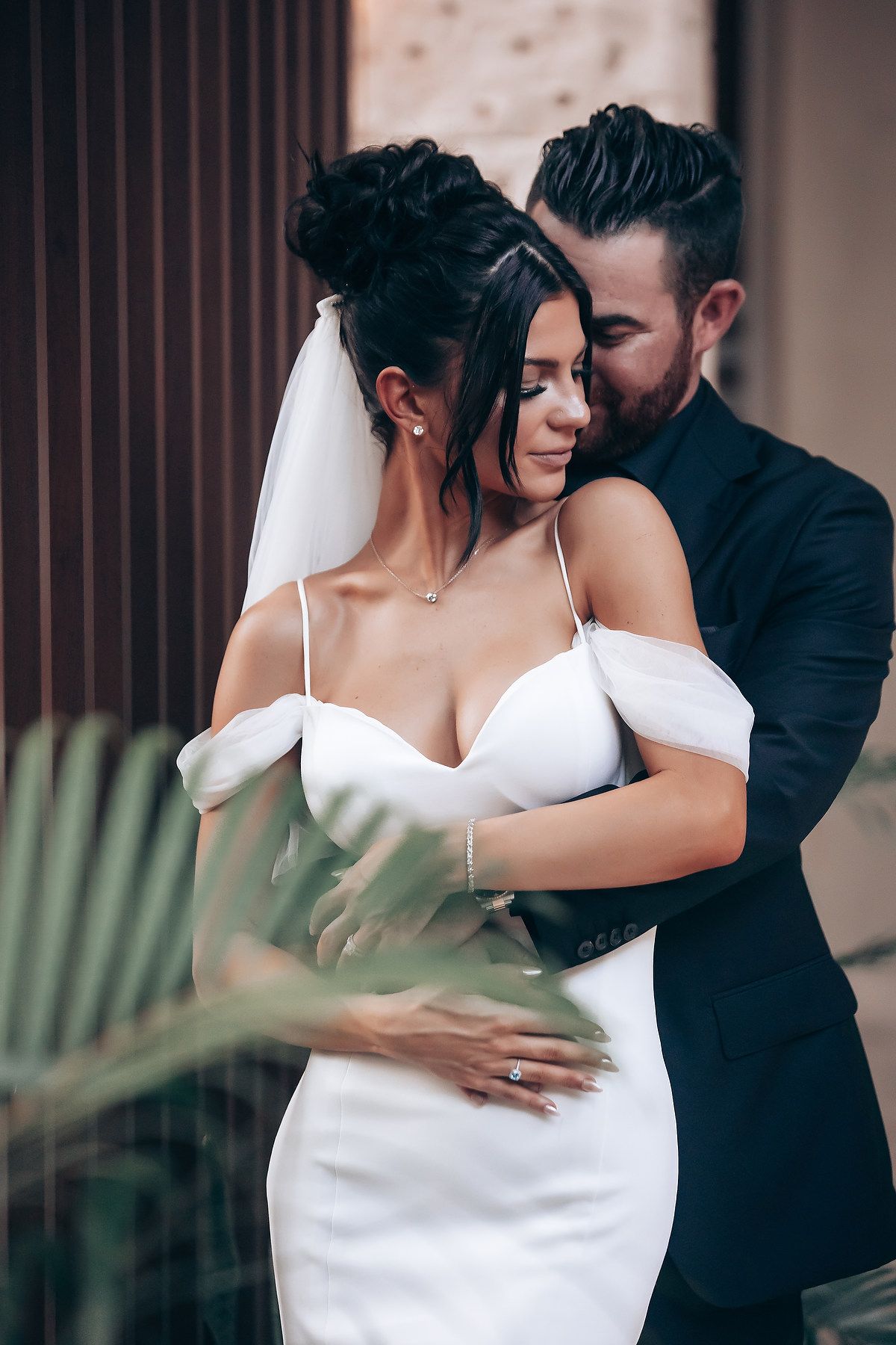 Romantic wedding couple embraces in intimate moment against dark wooden backdrop.