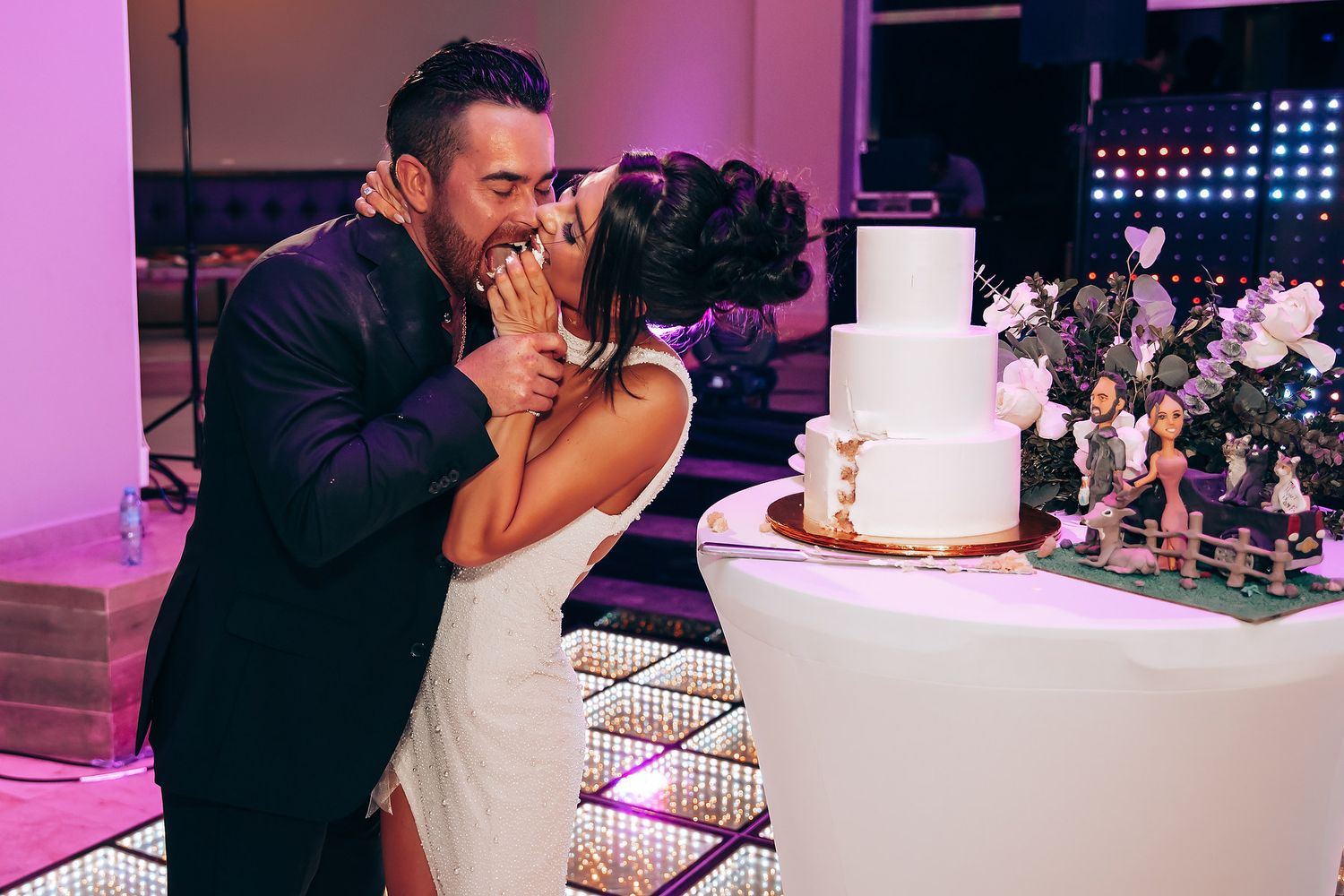 Wedding reception moments captured with purple lighting and white wedding cake display.