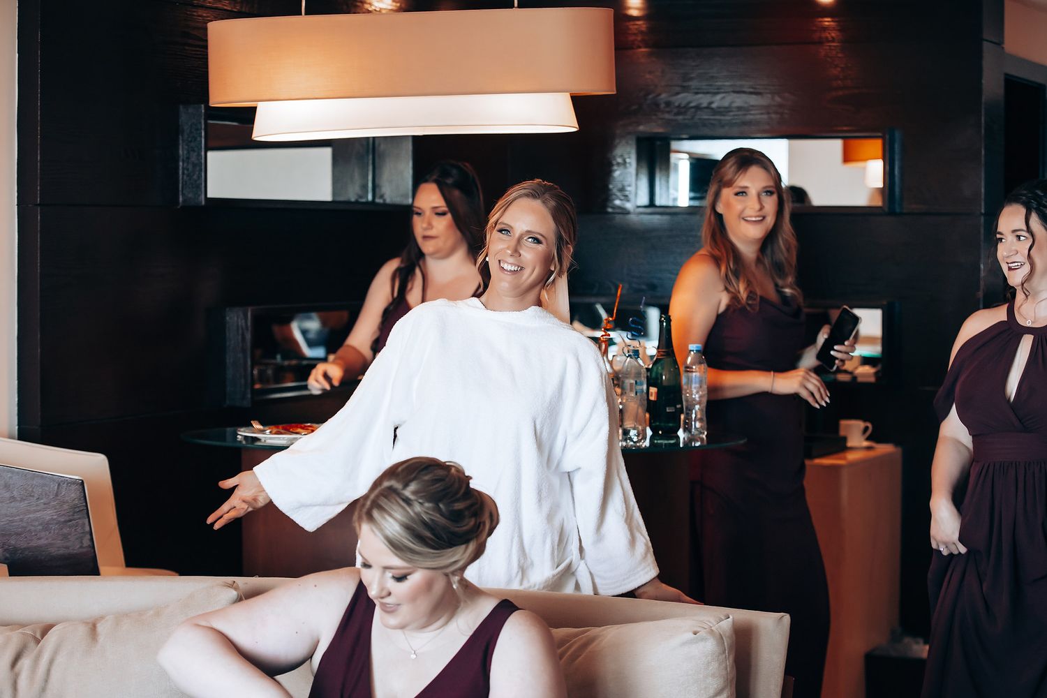 A group of women sitting and standing in a dimly lit room, with a chandelier and furniture visible.
