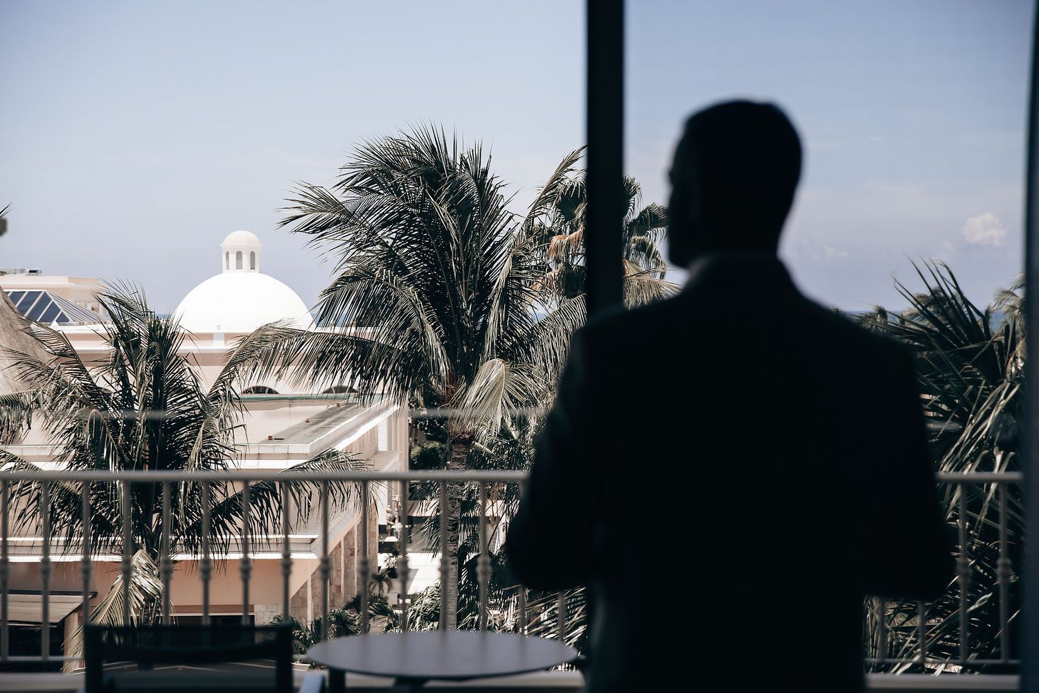 A silhouetted figure stands in front of a building with palm trees.