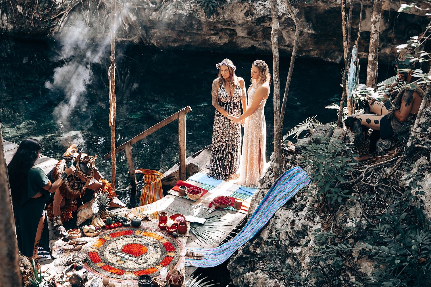 Two women in long dresses standing on a table in a forest setting.