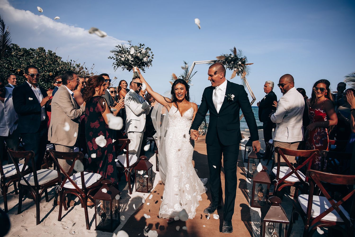 Wedding ceremony guests gathered outdoors under blue skies for a celebration.