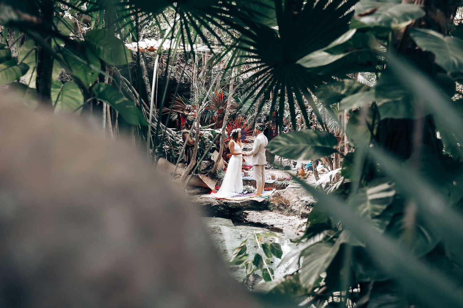 Tropical palm fronds frame an outdoor wedding ceremony in a natural forest setting.