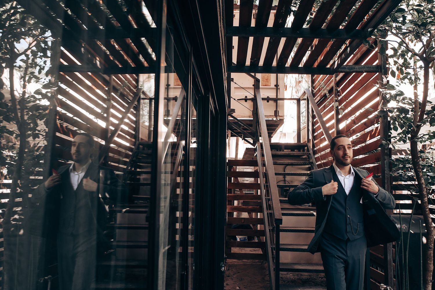 Person in formal attire stands between wooden slats creating dramatic shadows and lighting effects.