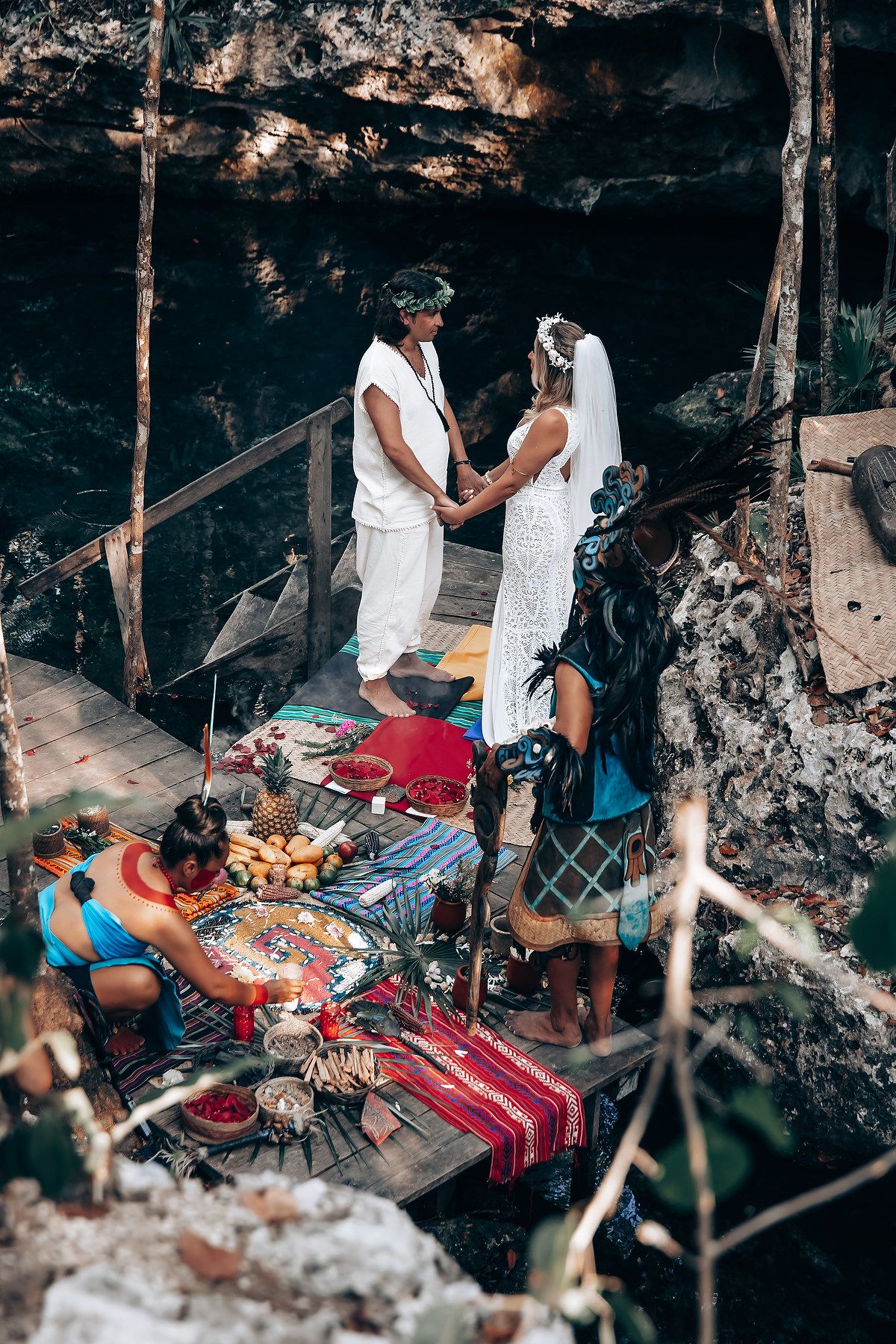 A couple celebrates their wedding ceremony with a picnic spread on blankets inside a rocky cave setting.