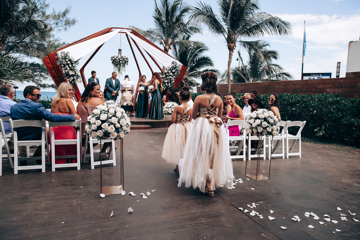 White folding chairs line a beachside wedding venue with palm trees in the background.