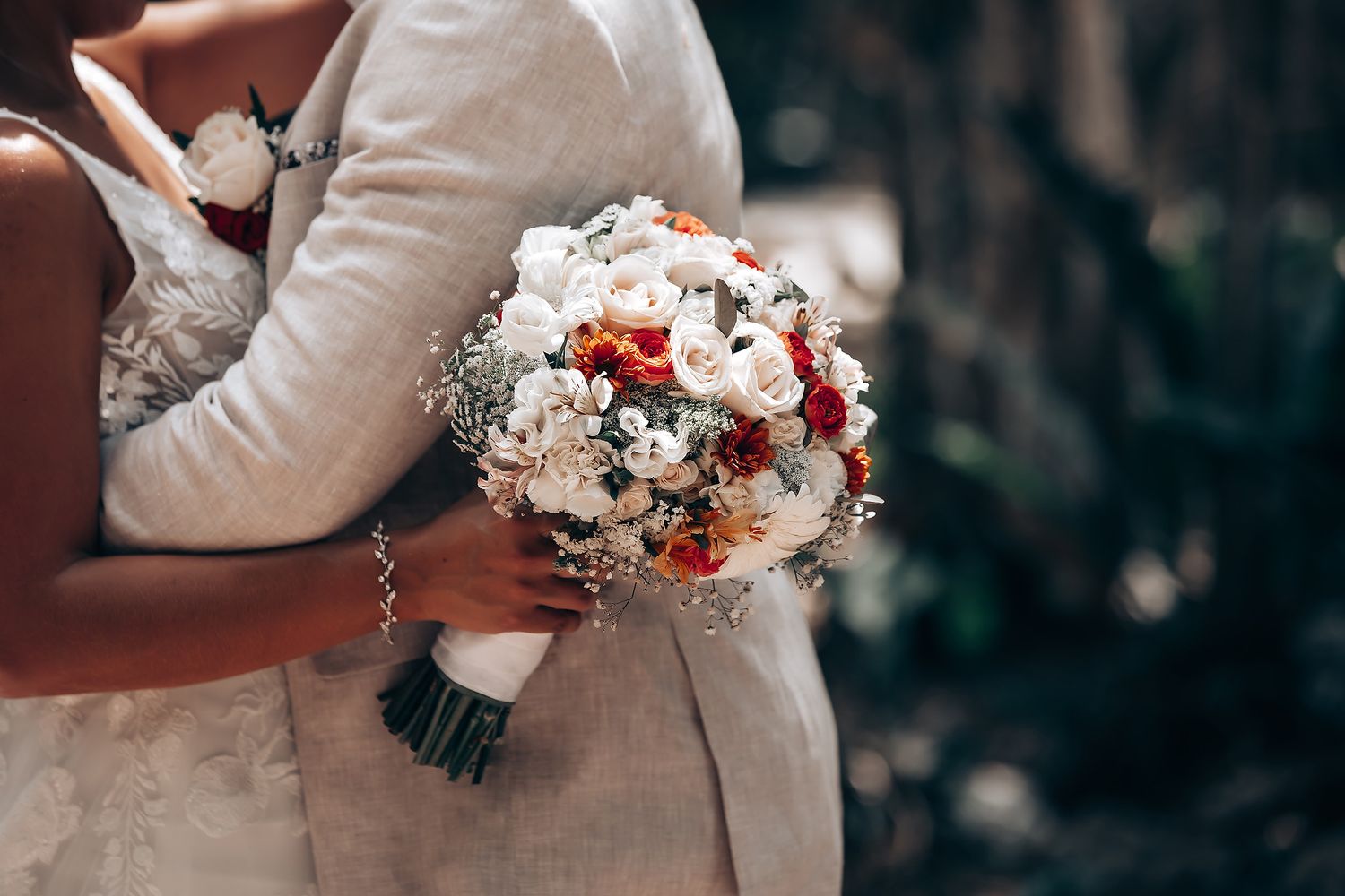 Wedding couple holding beautiful red and white floral bouquets in an outdoor setting.
