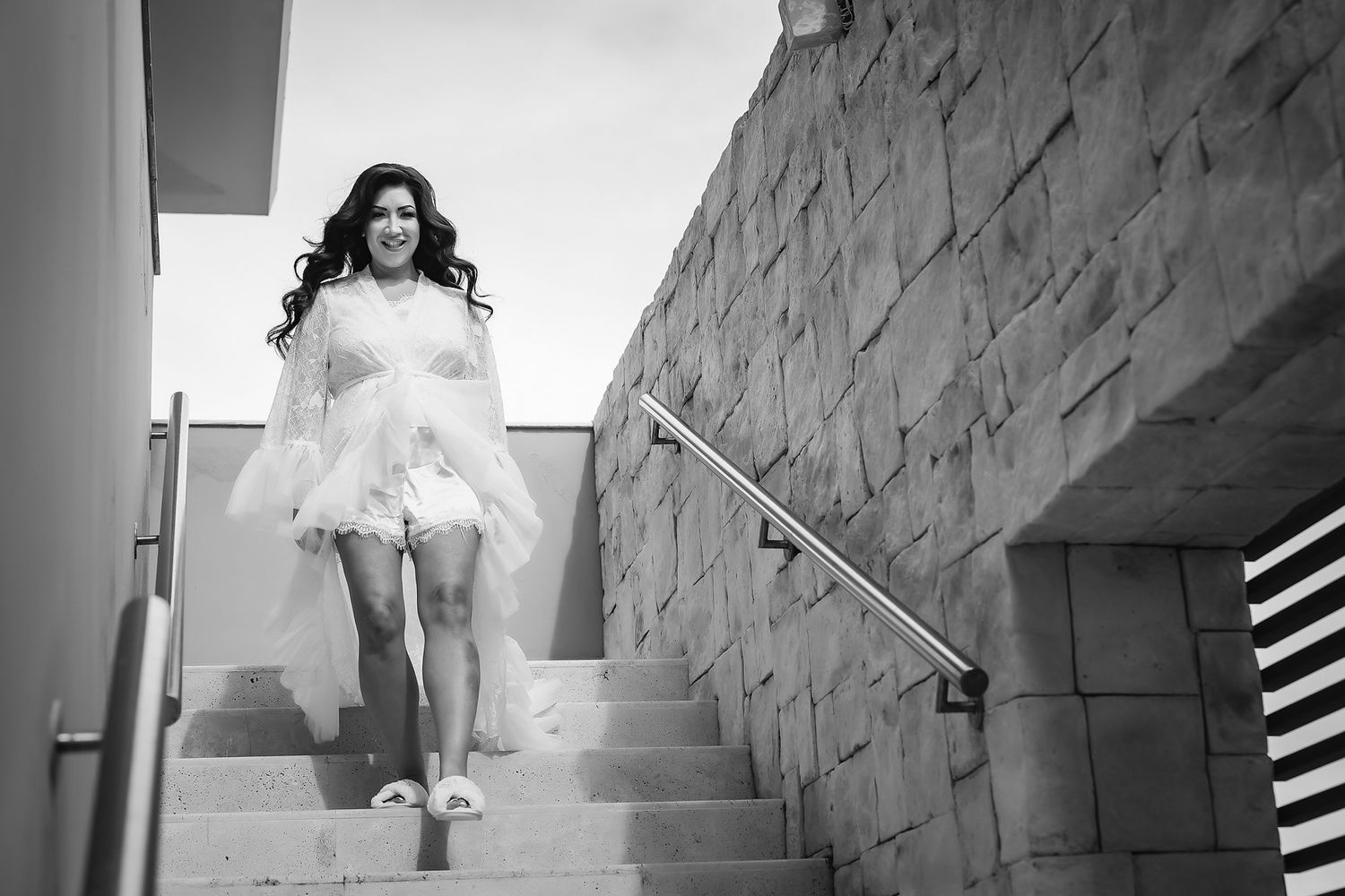 Black and white photo of a woman in a white dress descending outdoor stone stairs with a metal railing.