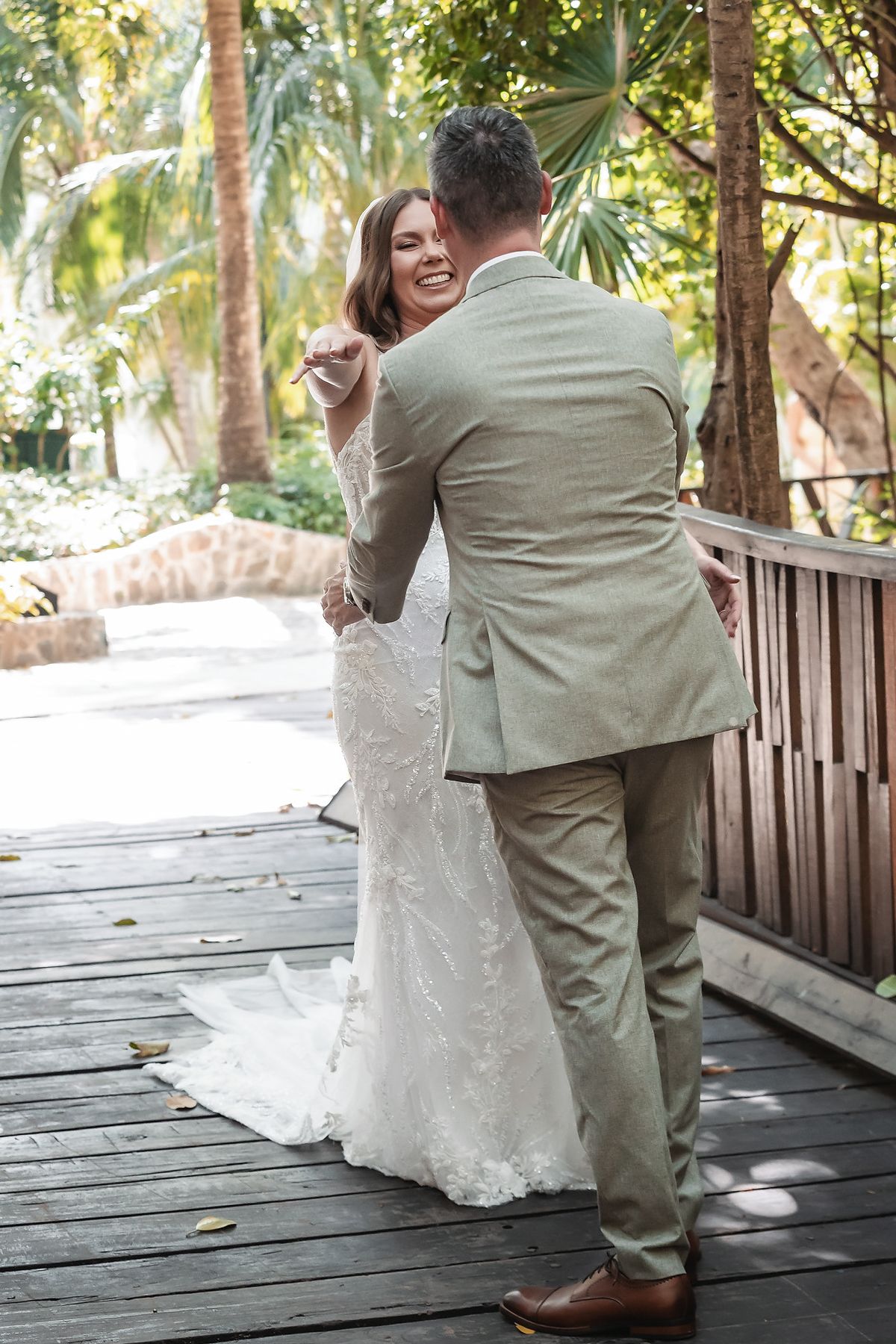 Bride and groom share a joyful dance on a wooden deck surrounded by lush tropical greenery.