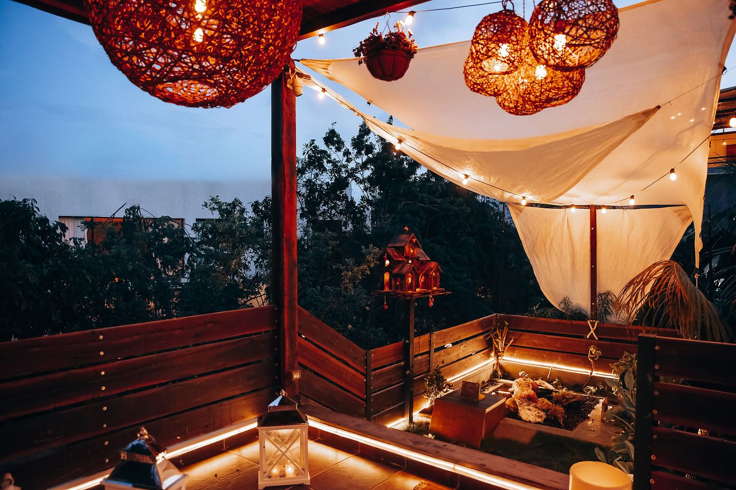 Romantic rooftop lounge at dusk with glowing wicker lanterns, string lights, and cozy seating area.