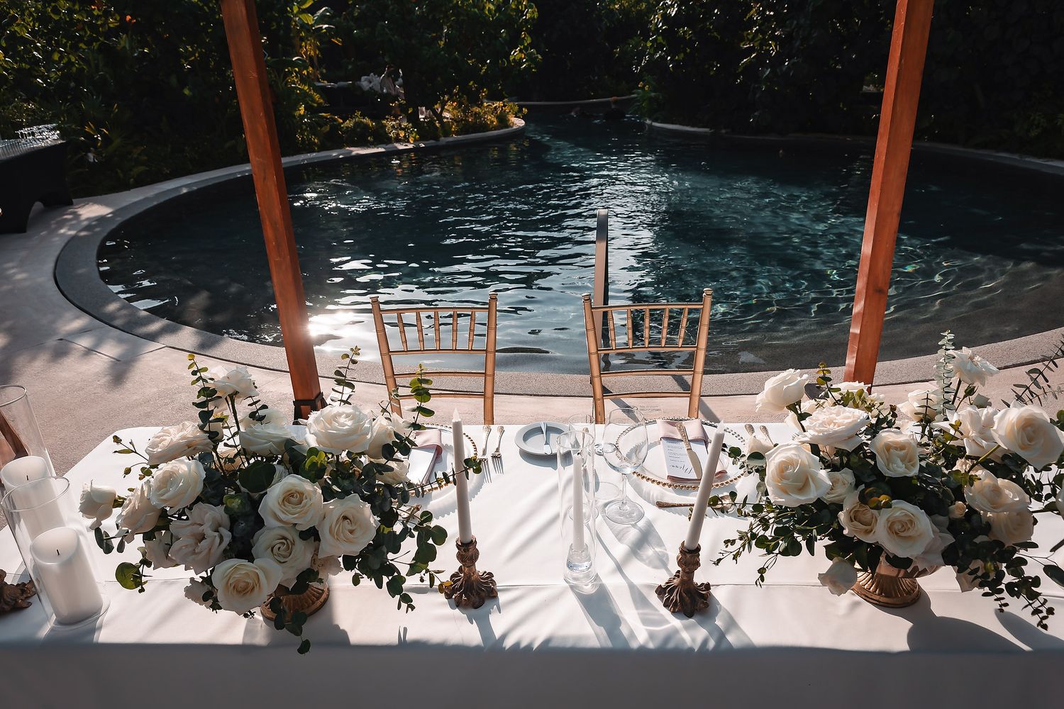 Elegant poolside wedding sweetheart table adorned with white roses and greenery at a luxury outdoor venue.