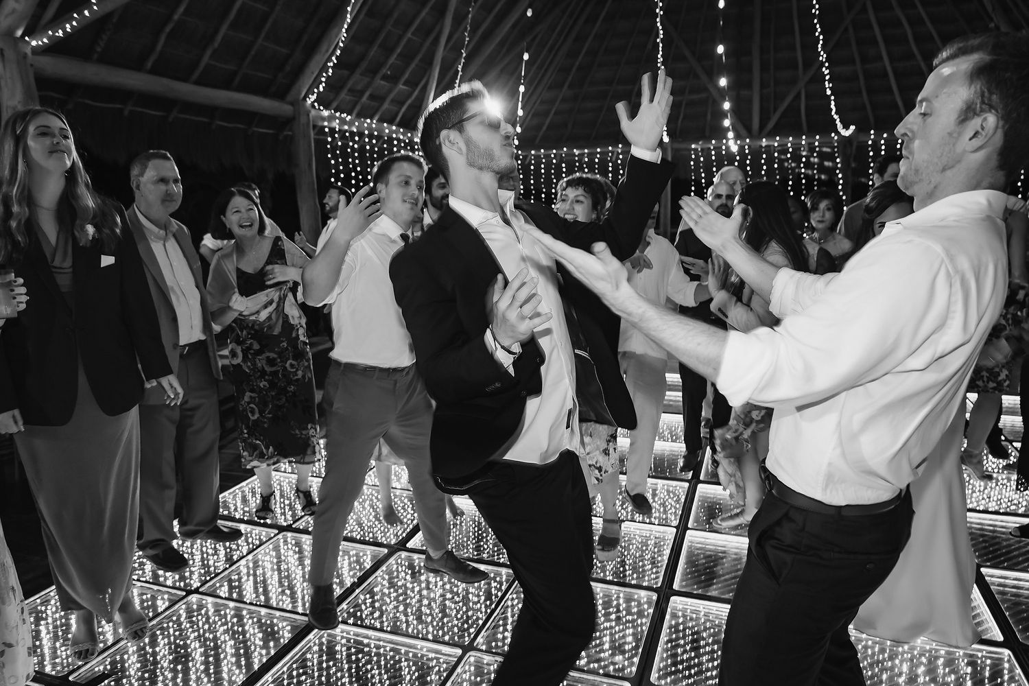 Black and white photo of groom and guests dancing energetically at wedding reception.