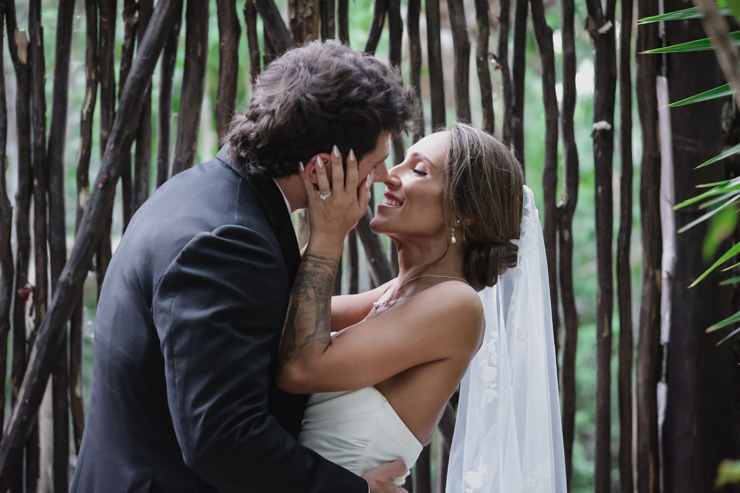 A bride and groom share a romantic kiss surrounded by rustic wooden branches during their outdoor wedding ceremony.