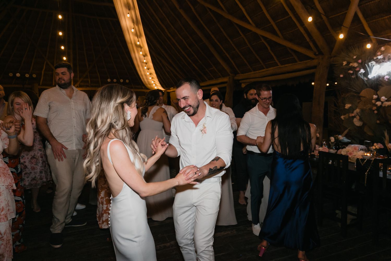 Bride and groom dancing joyfully with guests at lively tropical wedding reception celebration.