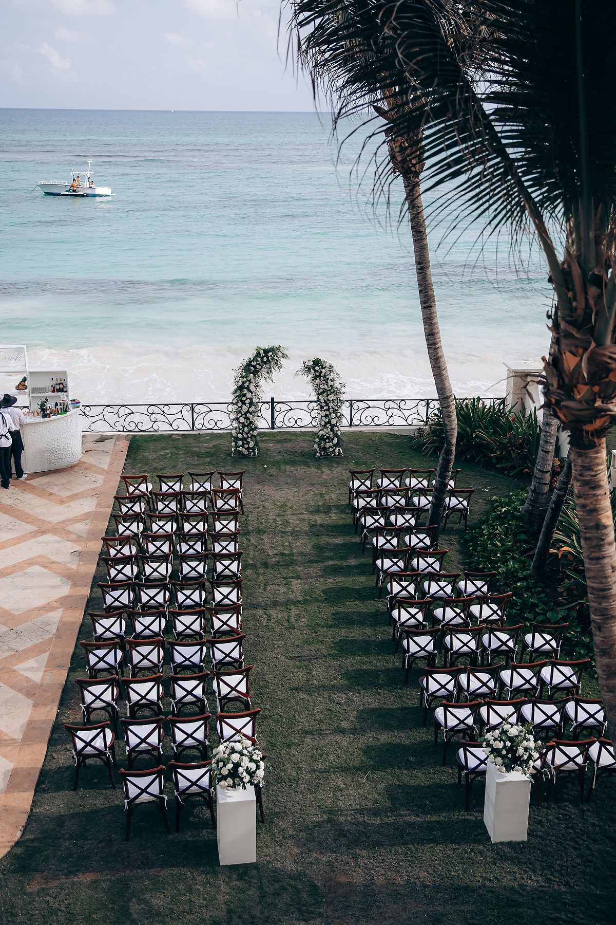 Beachfront wedding ceremony setup with white chairs facing the ocean and palm trees.
