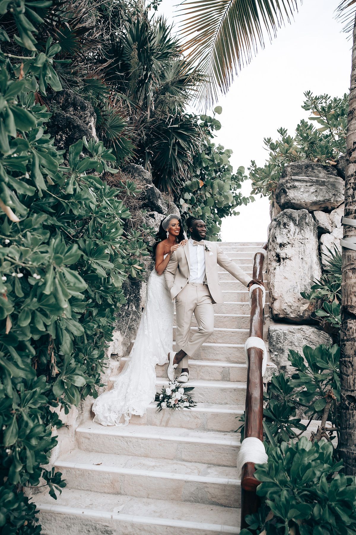 Wedding couple ascending stone steps surrounded by lush tropical greenery.