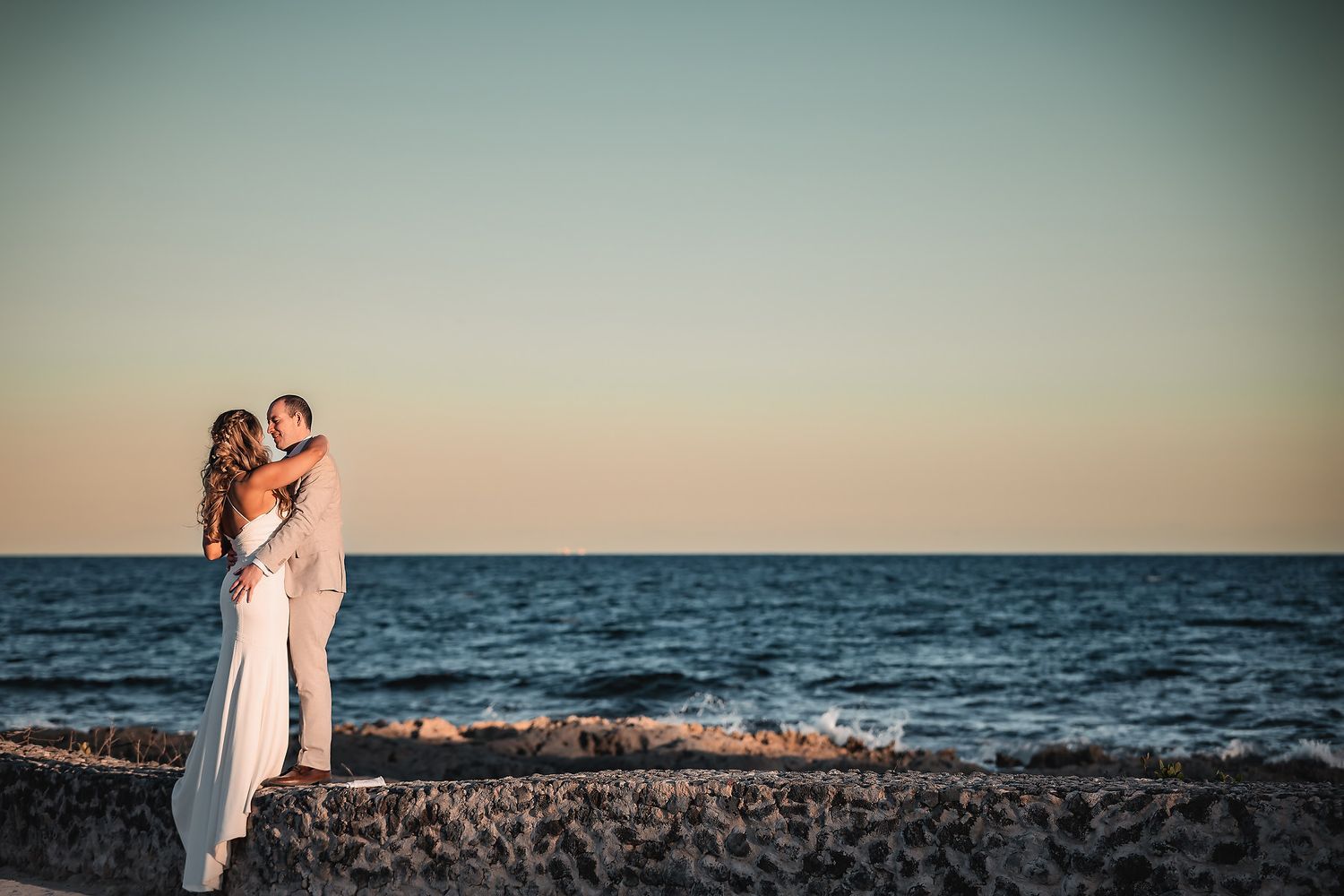 Romantic beach wedding photoshoot with ocean waves and sunset in the background.