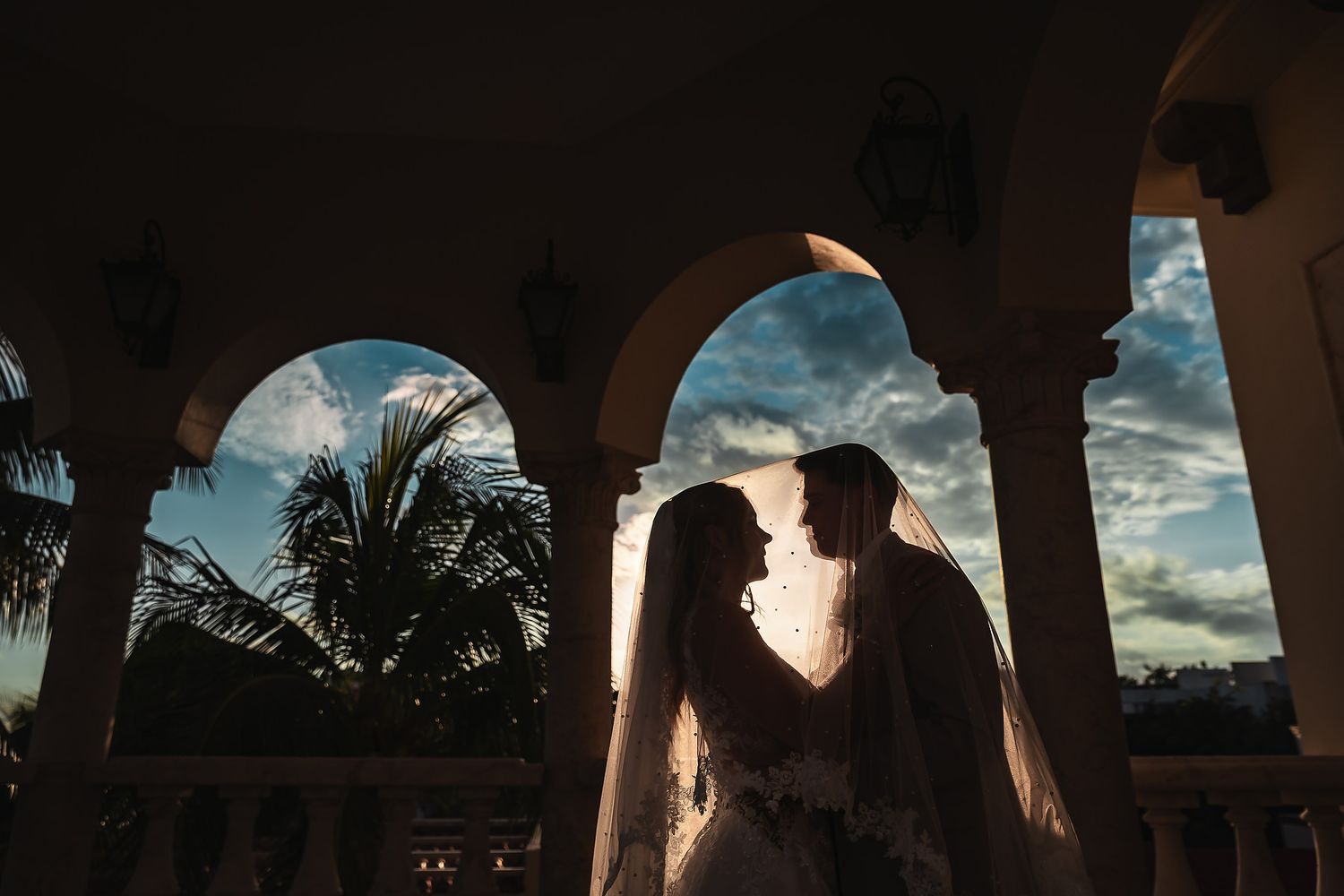 Tropical beach wedding ceremony setup with white chairs and floral arrangements at sunset.