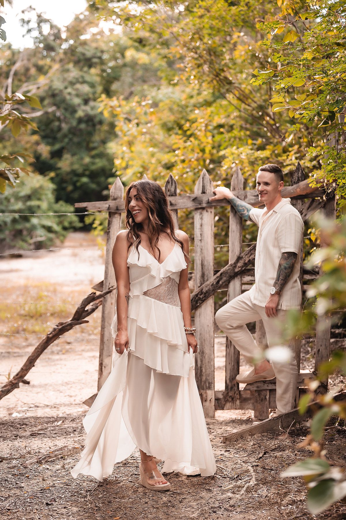 Ethereal outdoor portrait with flowing white dress and casual wear against natural wooden fence.