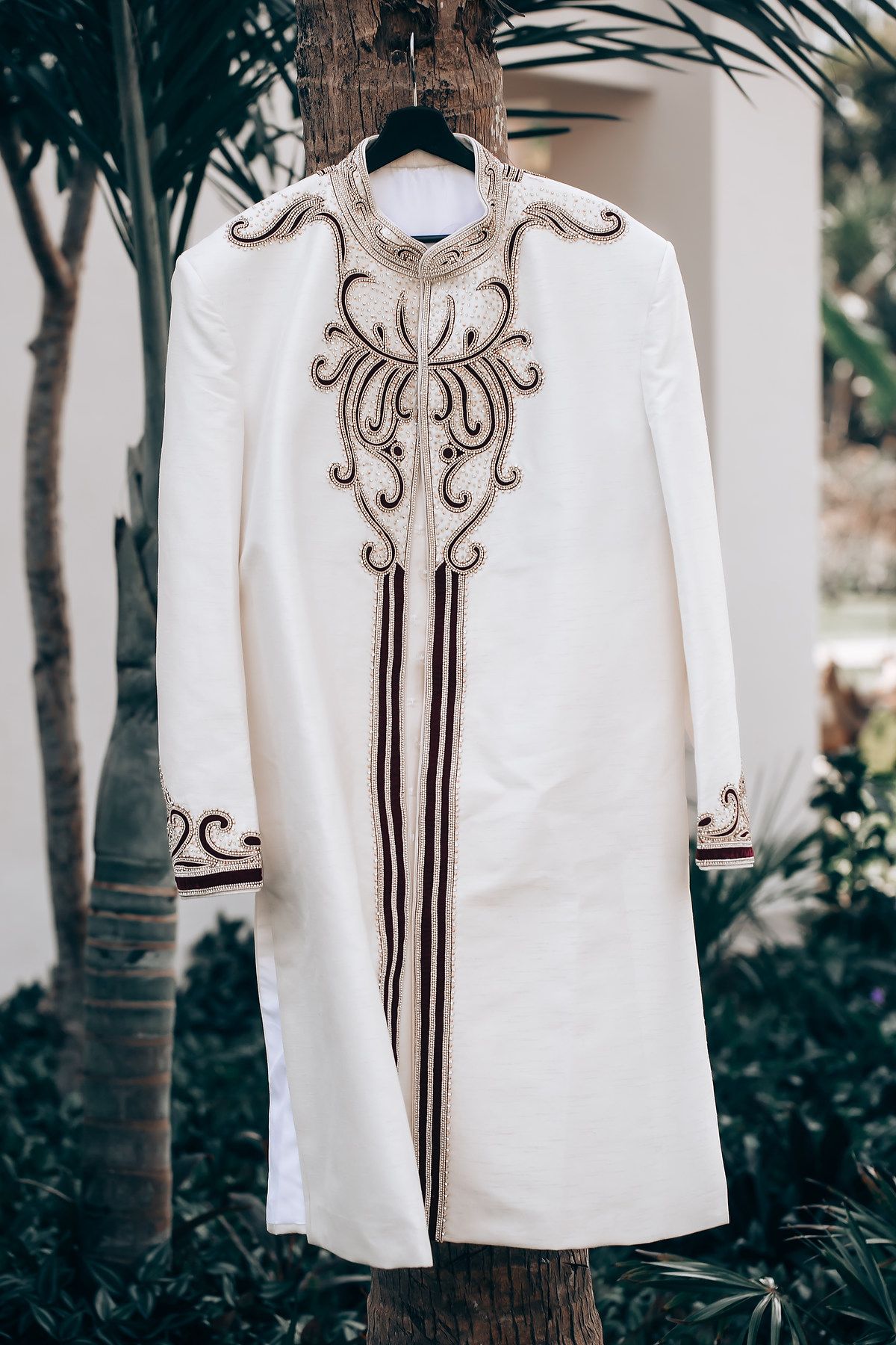 White traditional wedding attire with intricate gold embroidery details hanging outdoors.