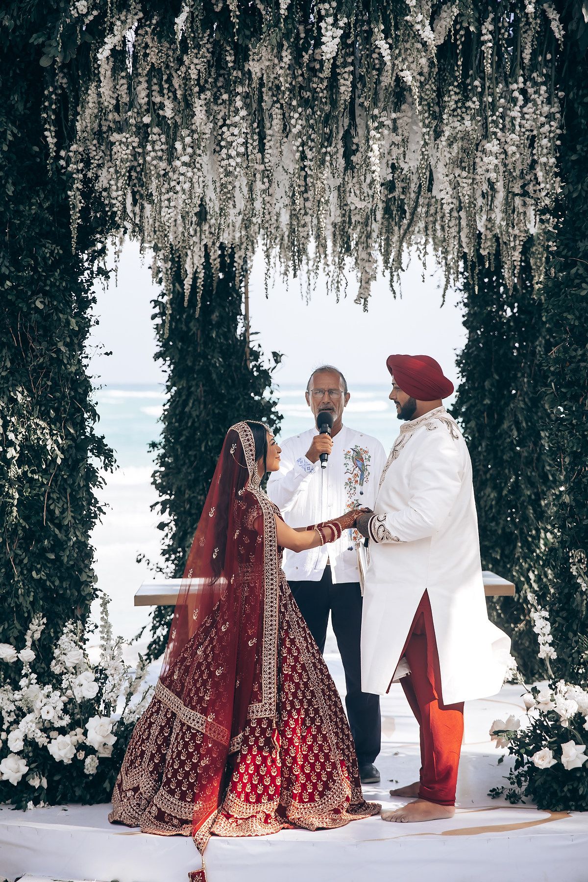 Beach wedding ceremony with traditional Indian attire and decorative floral arrangements.