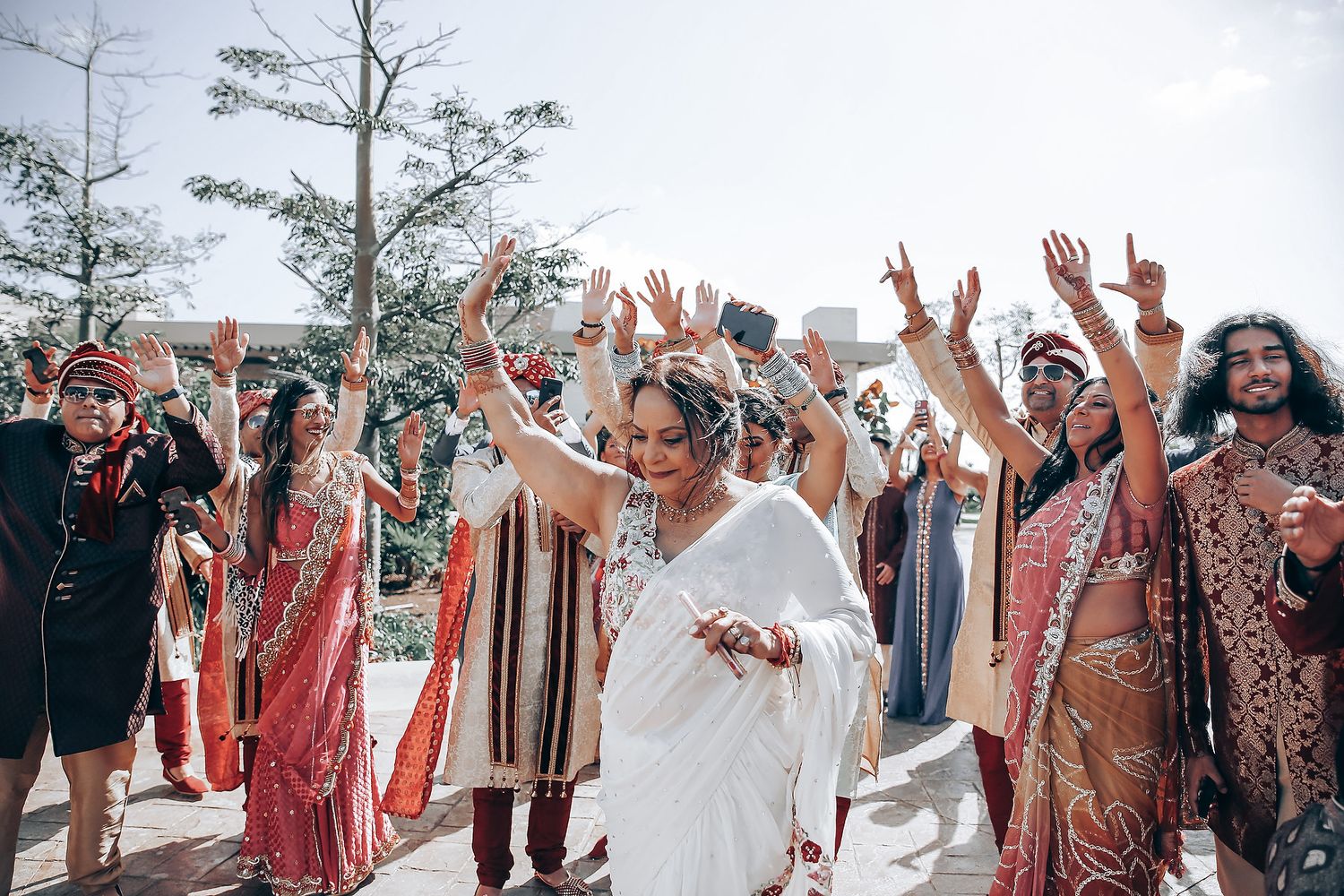 Joyful celebration at an outdoor Indian wedding with guests in colorful traditional attire.