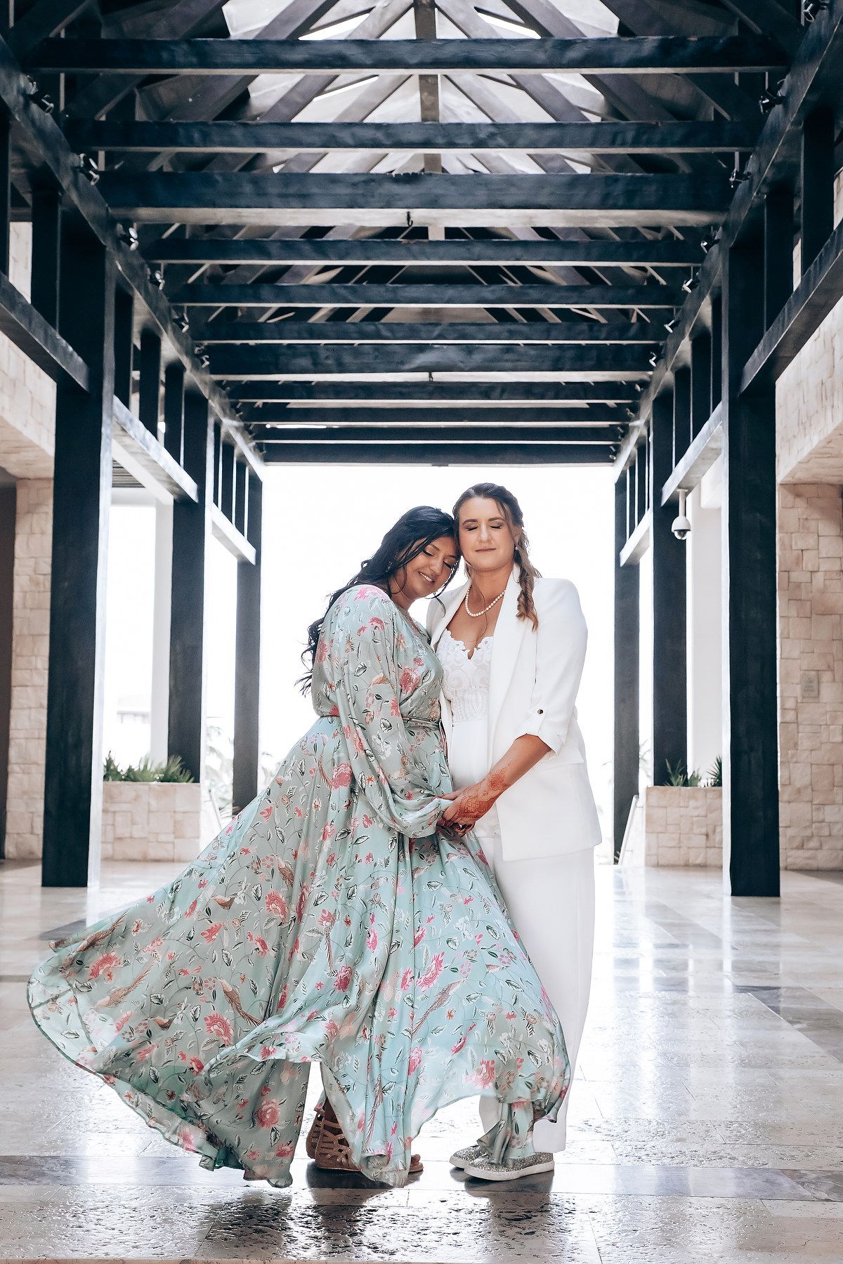 A couple poses in a covered walkway, with the woman's floral dress flowing dramatically.