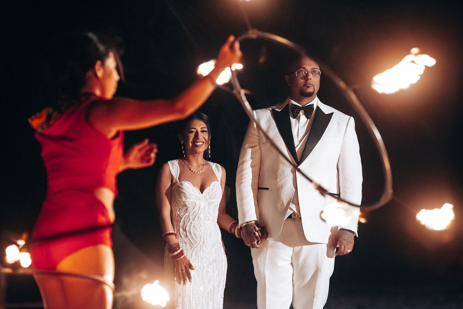 Fire dancers perform at a beachside wedding reception as newlyweds watch in formal attire.