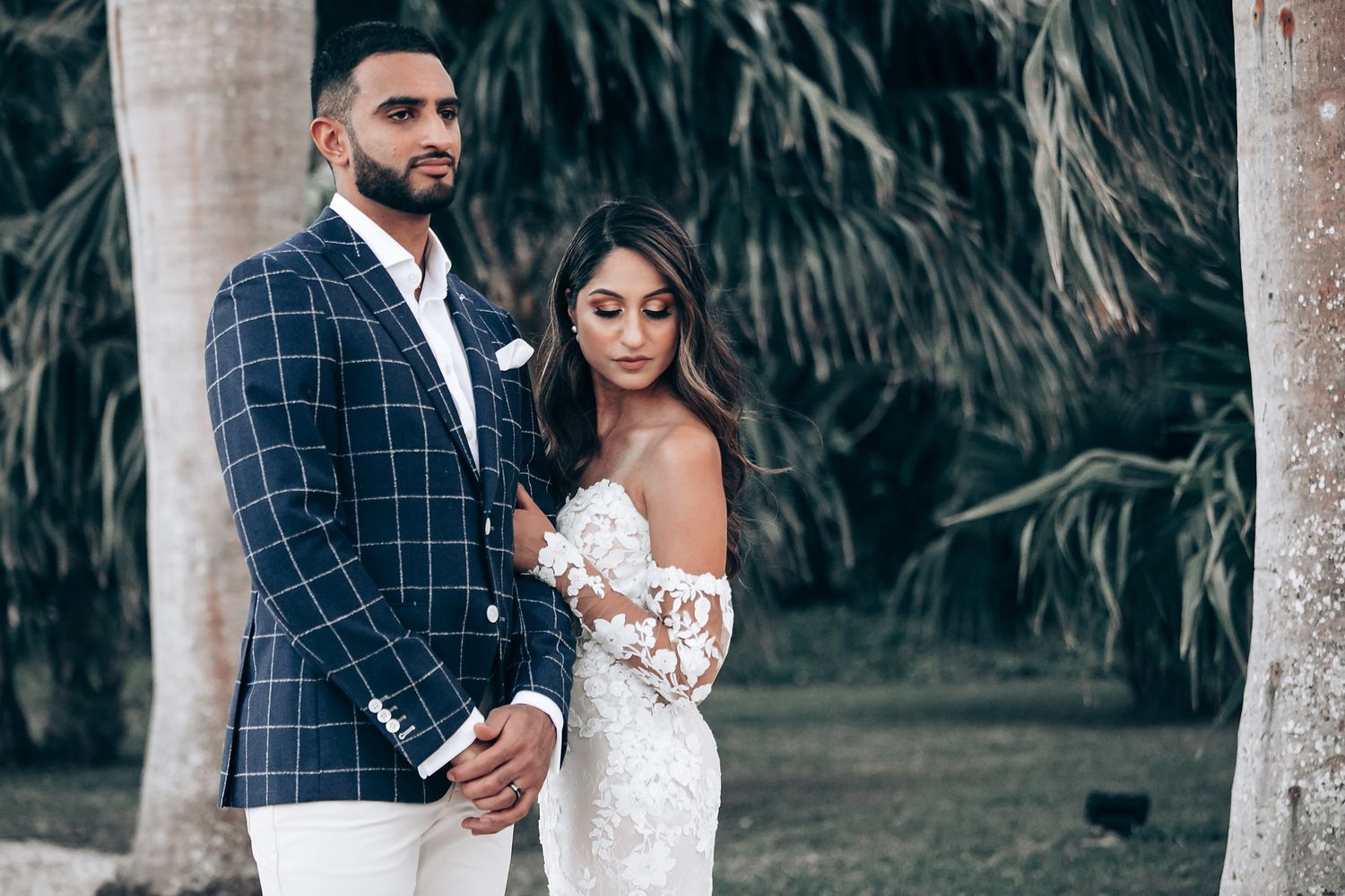 A couple shares an intimate moment in a lush garden setting wearing formal attire.