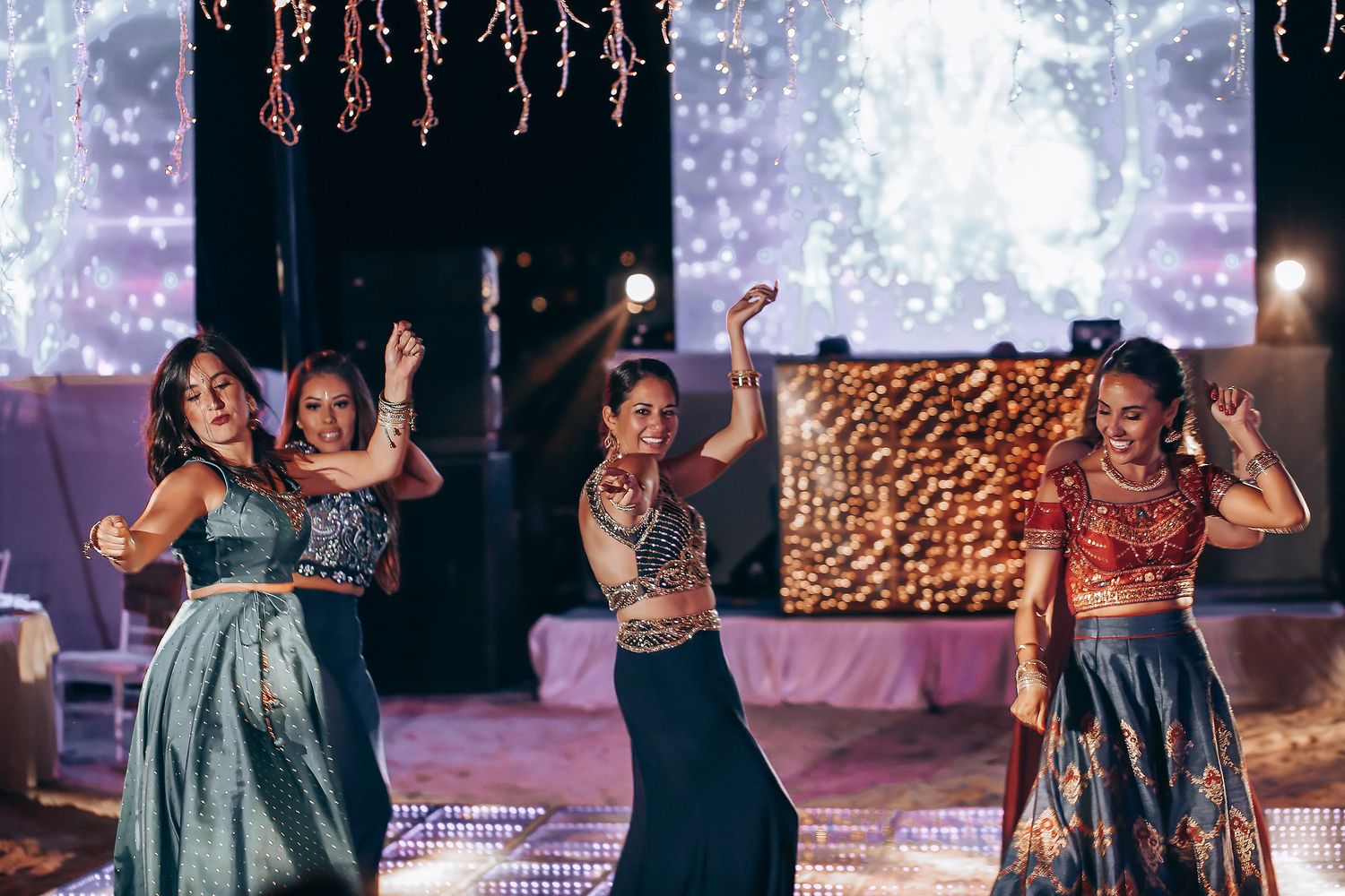 Performers dance energetically on a stage with dramatic purple lighting and sparkling effects in the background.