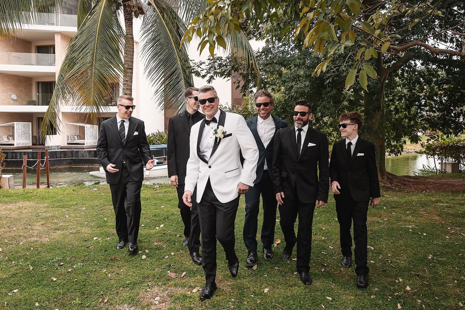 Wedding party walks through palm tree lined path in formal attire.