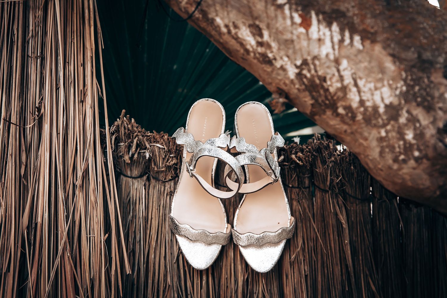 White wedding shoes and rings arranged artistically on a rustic wooden surface with hanging decorative elements.