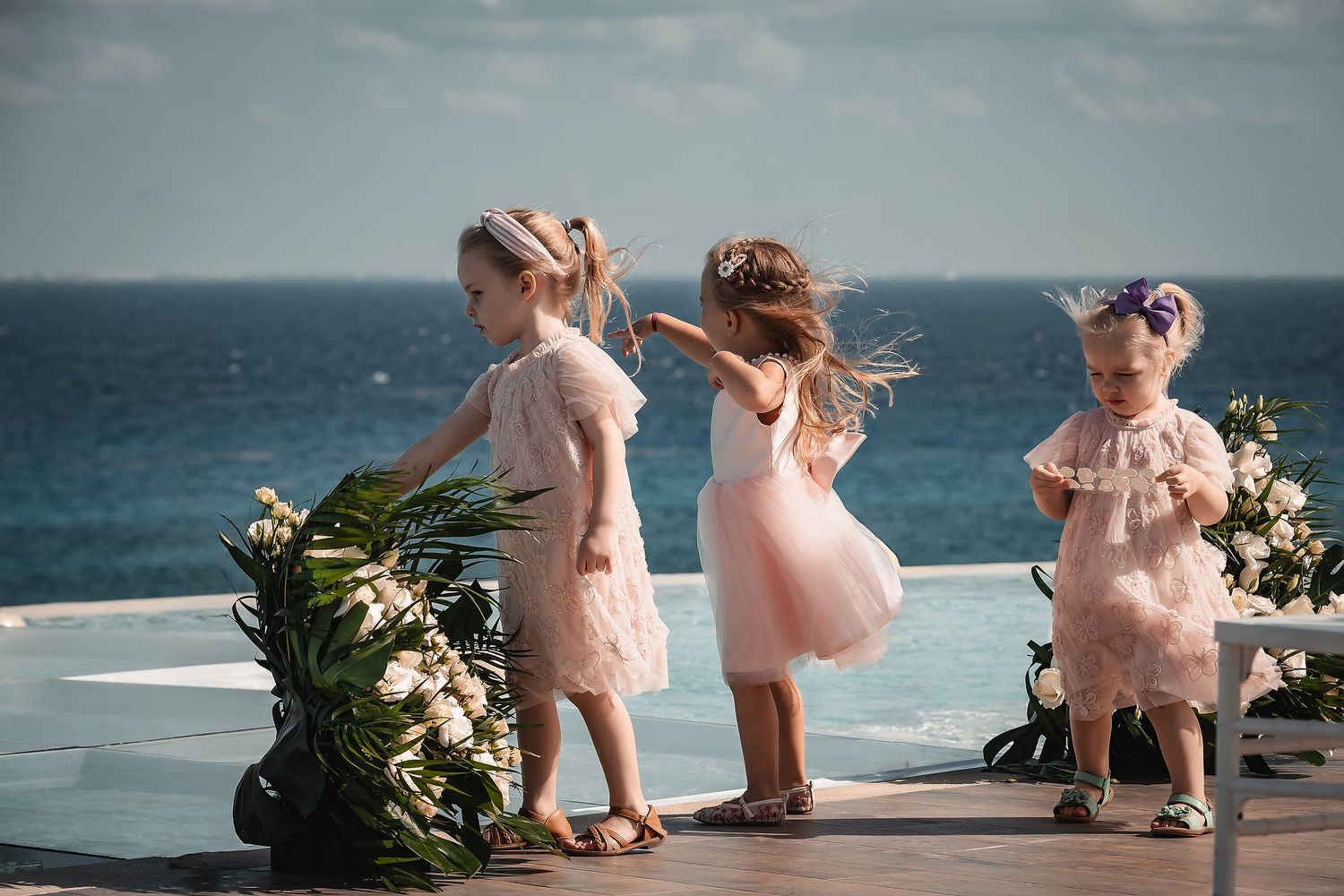 Young attendants in pink dresses walk along a scenic oceanfront path.