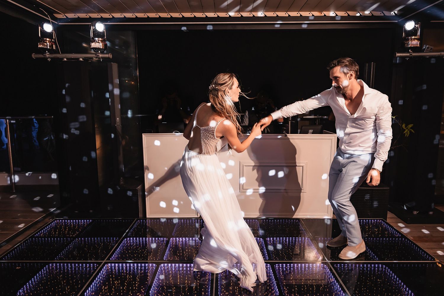 Couple dances energetically on illuminated dance floor during wedding celebration.