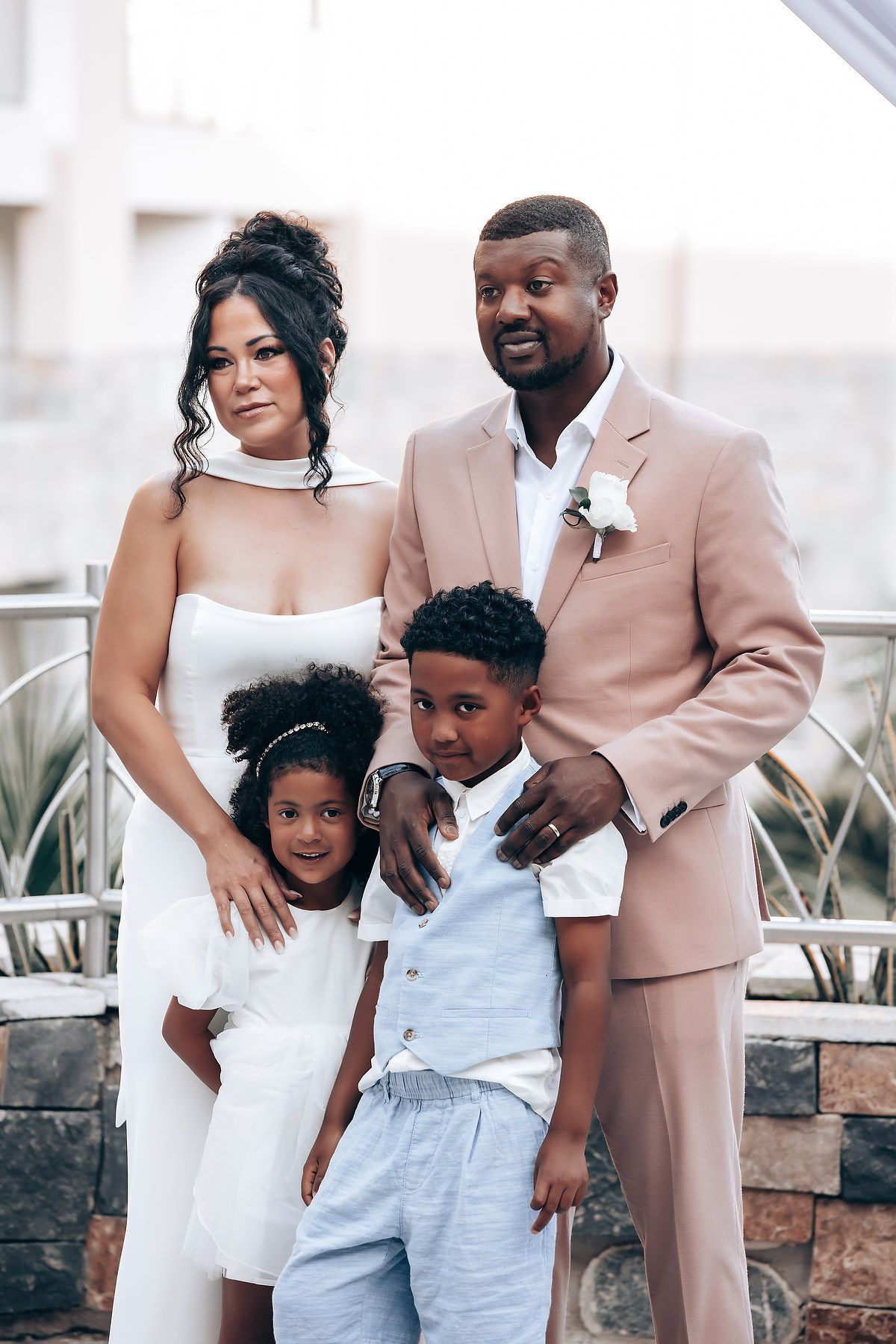 Family portrait on outdoor terrace with bride in white dress and guests in formal wear.